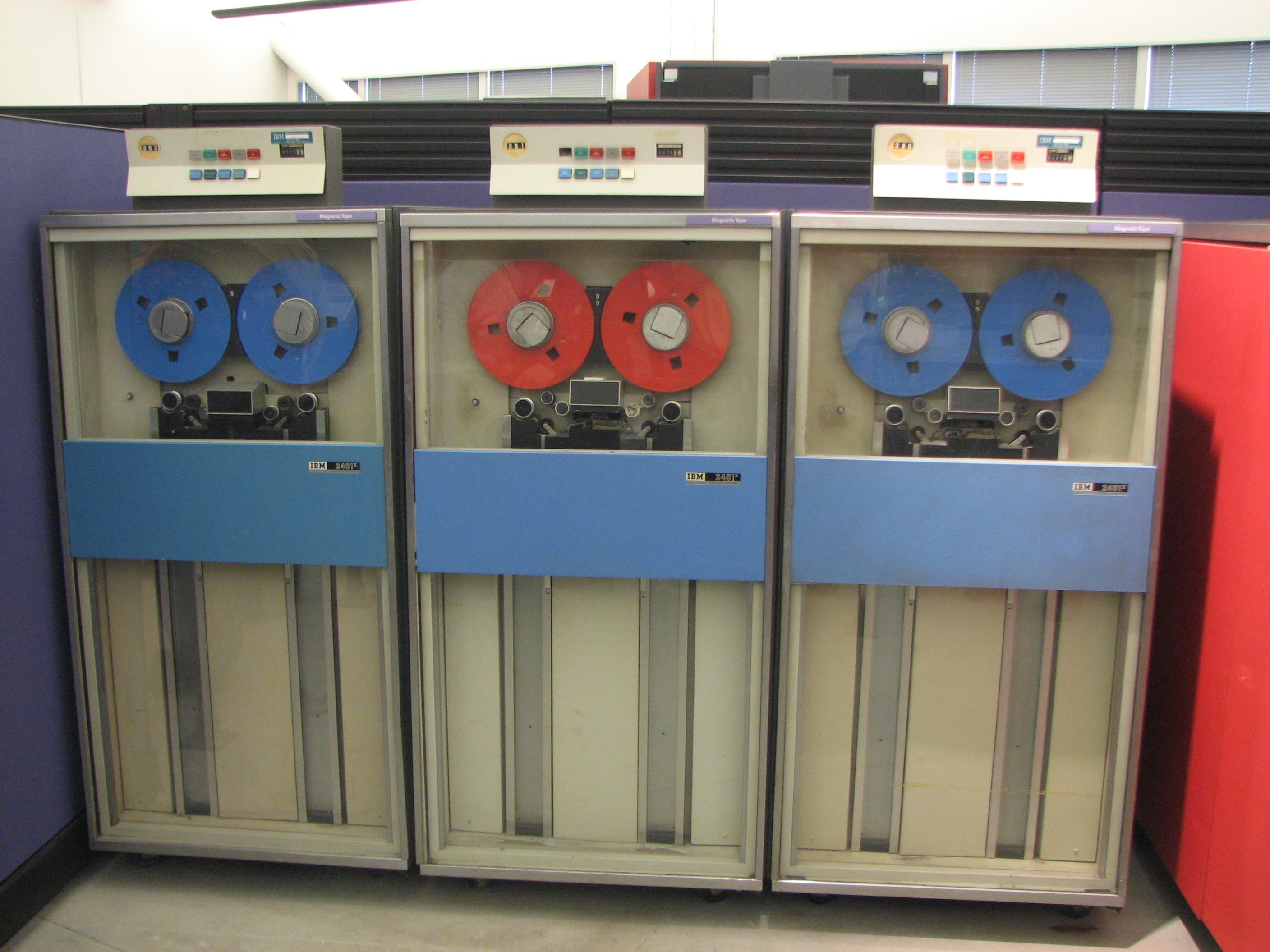 A row of IBM System 360 magnetic tape drives with large reels visible behind glass